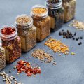 Assortments of spices, white pepper, chili flakes, lemongrass, coriander and cumin seeds in jars on grey stone background. Copy space